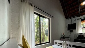 A bedroom with a large window, a bed with white bedding, a yellow pillow, and a white headboard.