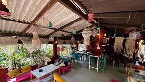 A restaurant with outdoor seating, tables, chairs, and hanging decorations.