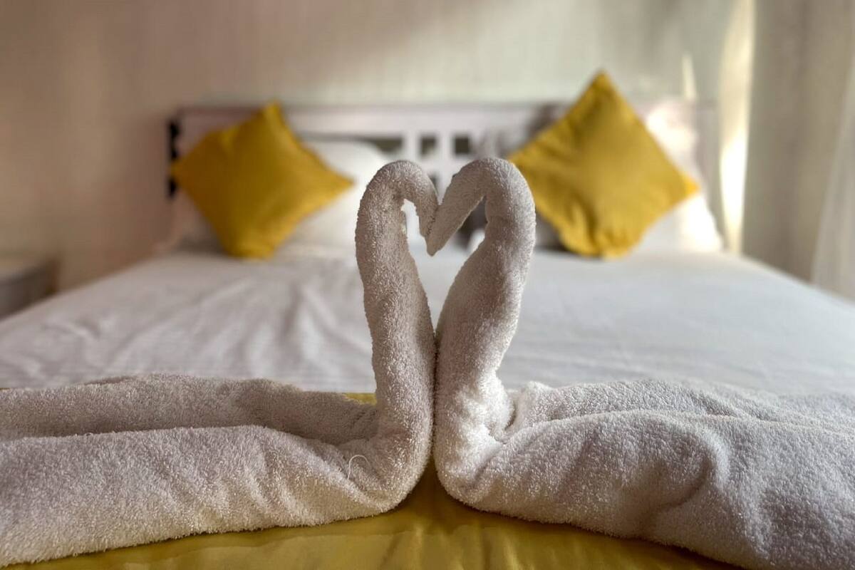 Una cama con sábanas blancas y dos toallas dispuestas en forma de corazón.