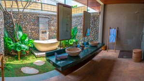 Un baño con pared de piedra, una bañera grande, un lavabo y un espejo.