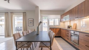 A modern kitchen with wooden cabinets, a built-in oven, and a dining area with a long table and chairs. - Superior 3BR Apartment in Chalandri (Chalandri)