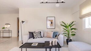 A modern living room with a white sofa, a coffee table, and a floor lamp. There is a framed artwork on the wall and a potted plant. - Superior 3BR Apartment in Chalandri (Chalandri)