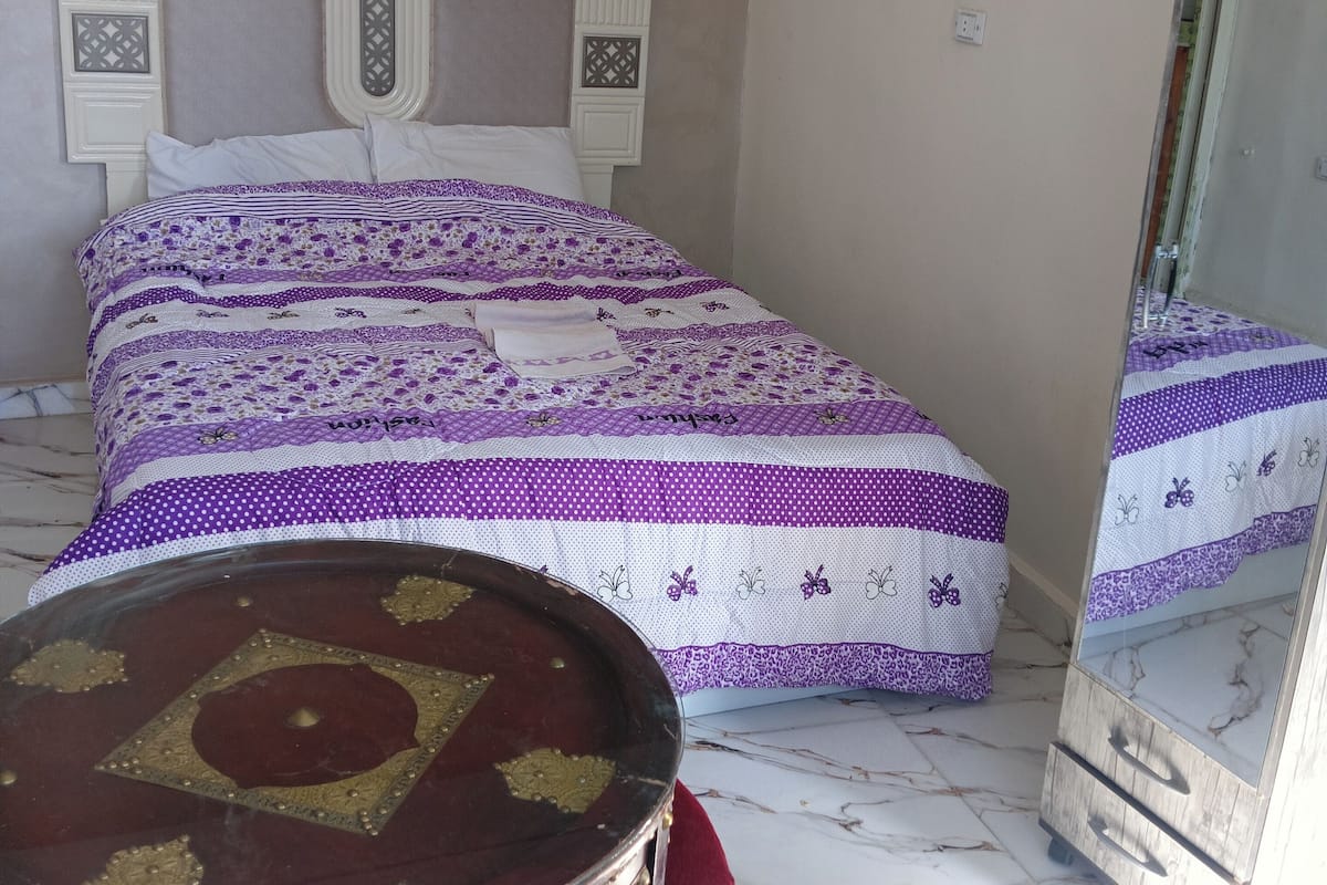A bedroom with a bed, a mirror, and a small table.