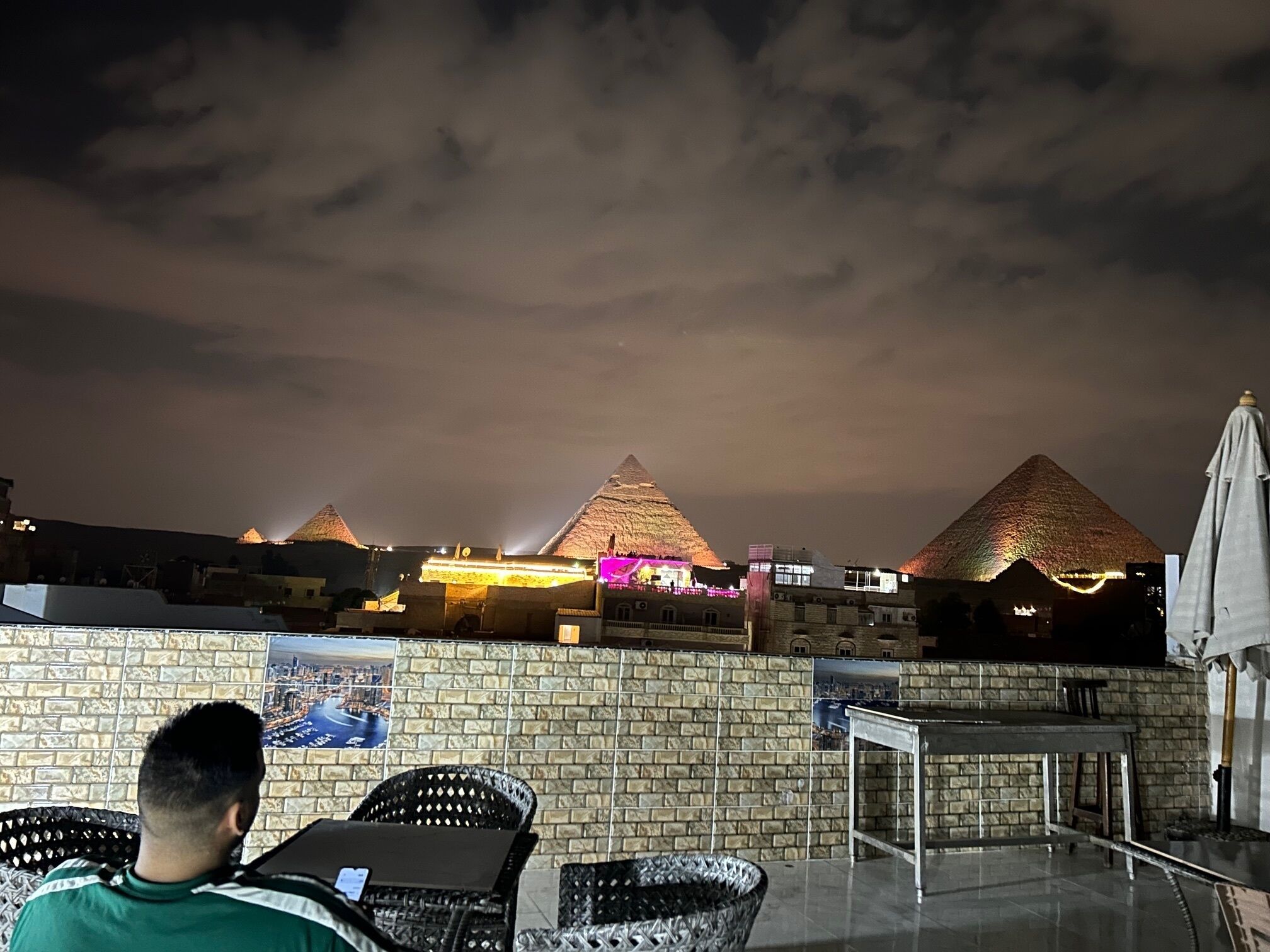 A rooftop terrace with a view of pyramids, wicker chairs, and a brick wall.