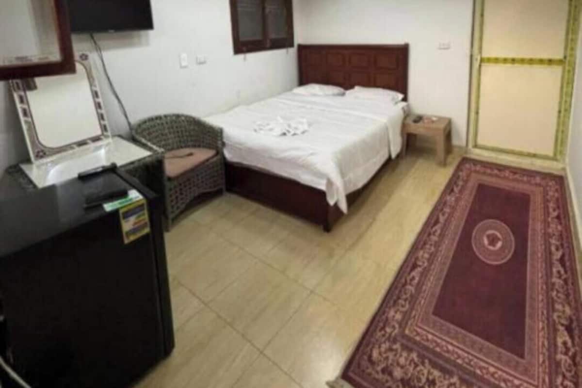 A bedroom with a bed, a desk, a chair, a TV, and a ceiling light fixture.