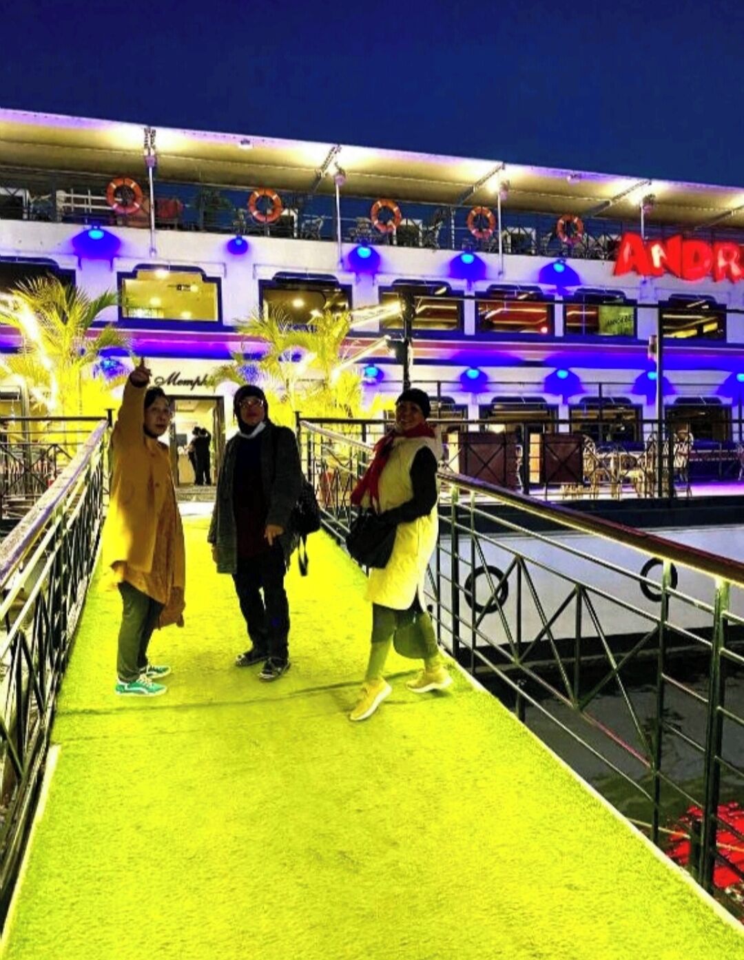 A brightly lit walkway with a yellow carpet leading to a building with multiple levels and a red sign.
