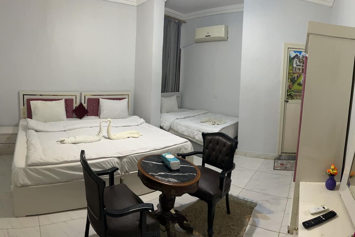 A hotel room with two beds, a small table, a chair, a TV, and a mirror.