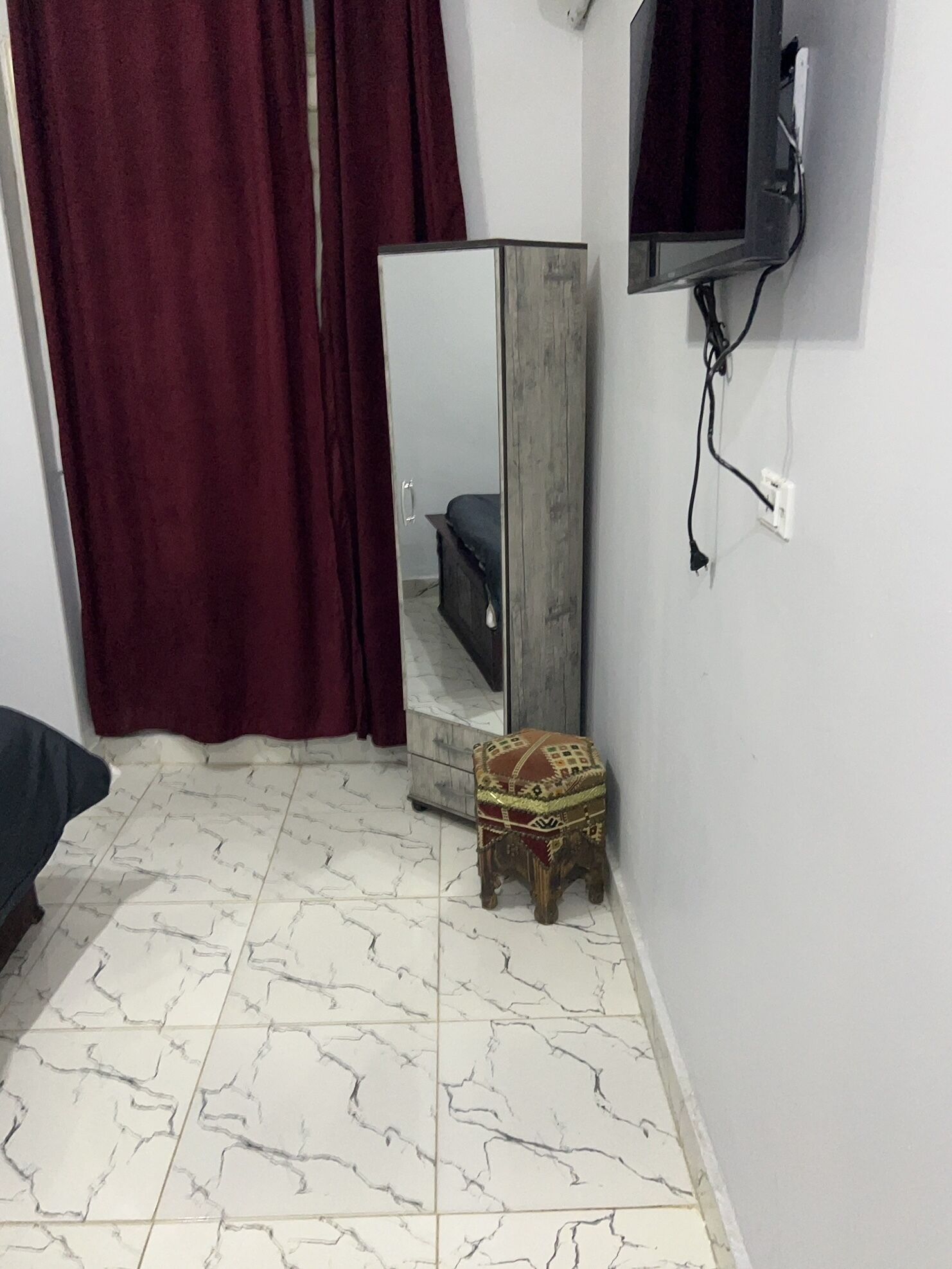 A bedroom with a bed, a mirror, a television, and a small stool.