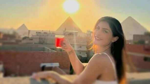 A person holding a cup, with a clear view of a pyramid in the background. - Falcon pyramids inn (Giza)