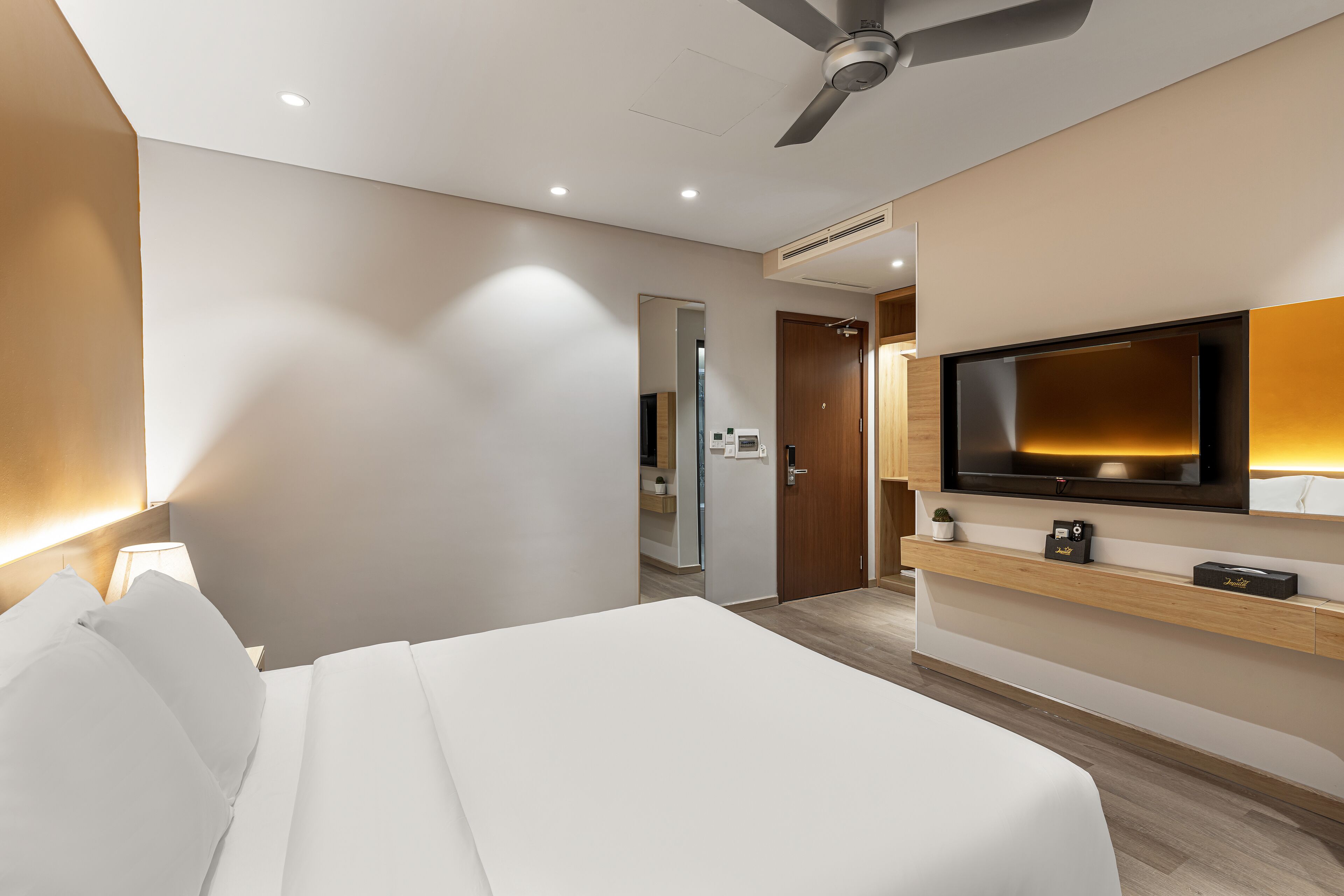 Une chambre d’hôtel moderne dotée d’un grand lit, d’un téléviseur à écran plat fixé au mur et d’un ventilateur de plafond.