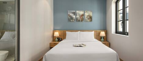 A hotel room with a bed, two bedside tables with lamps, a window, and artwork on the wall.