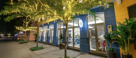 A building with a blue facade, large windows, and a tree with string lights.