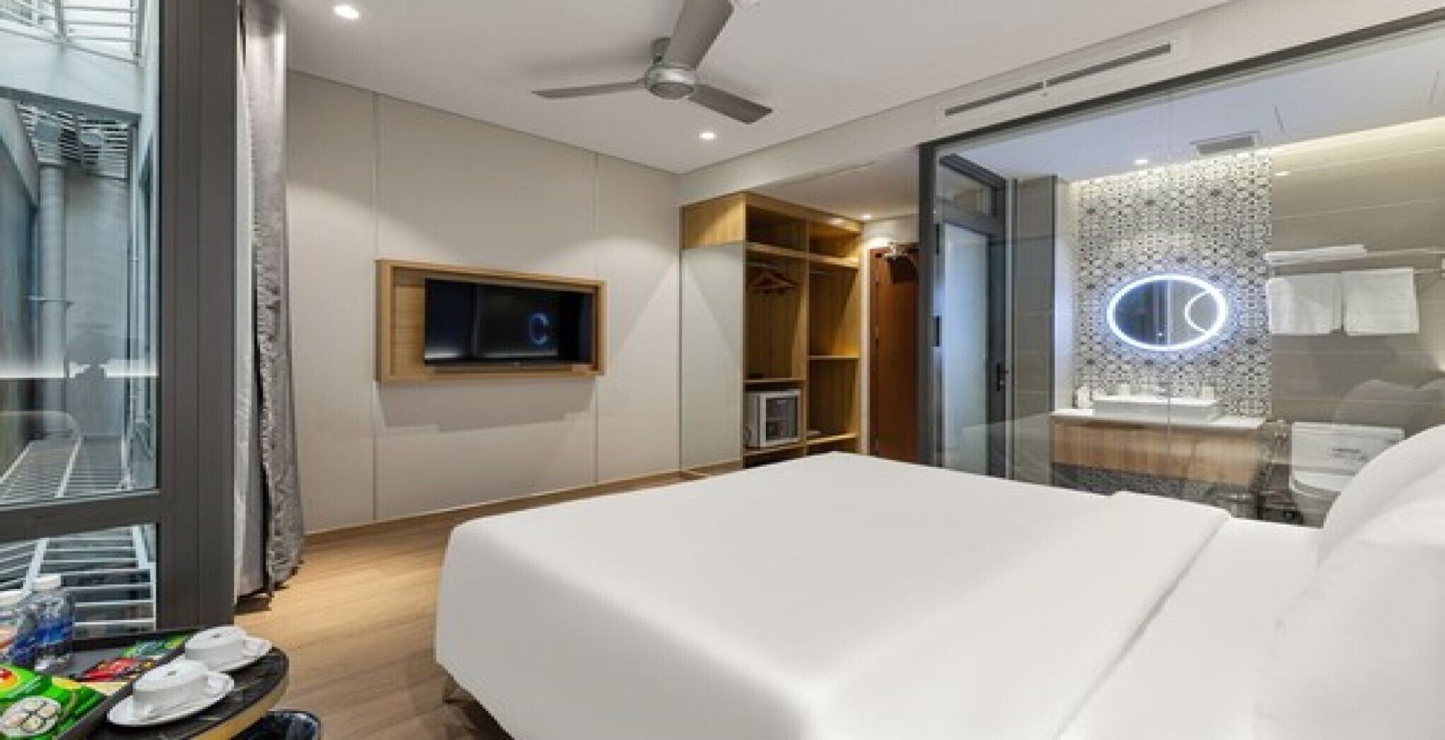 Quarto de hotel com cama, televisão na parede, guarda-roupa e casa de banho com espelho e iluminação.