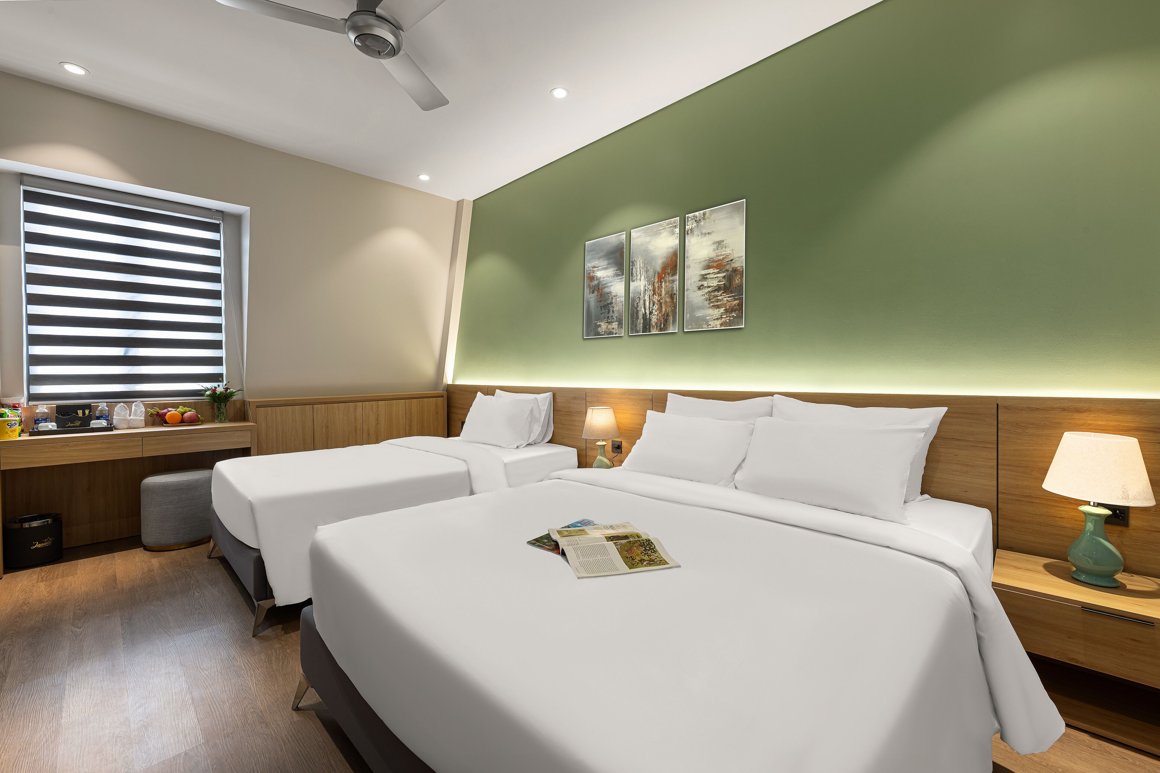 Habitación de hotel con dos camas, un escritorio con lámpara y obras de arte en la pared.