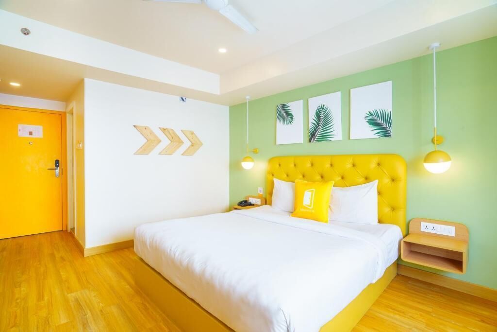 A room with a bed, a yellow headboard, a wooden nightstand, and a wall with three leaf prints.
