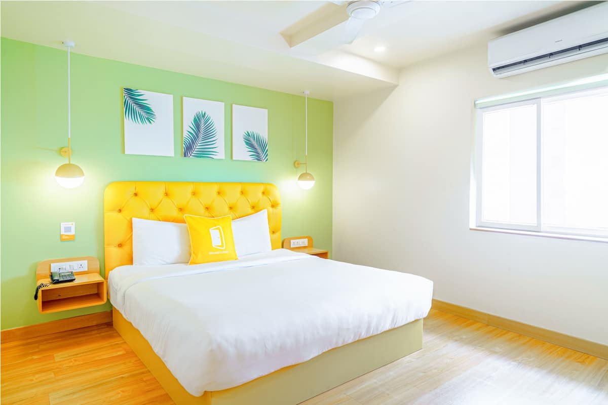 Habitación de hotel con cabecera amarilla, ropa de cama blanca y un ventanal grande que proporciona luz natural.