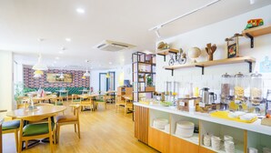 A modern cafe with wooden tables and chairs, a counter with food and drink dispensers, and shelves with kitchen utensils. - Bloom Hotel - Cyber Towers (Hyderabad)