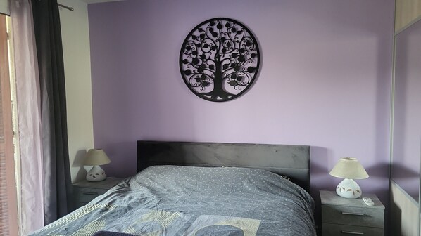 A bedroom with a bed, a nightstand, a lamp, and a wall decoration.
