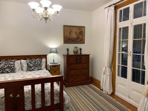A bedroom with a bed, dresser, lamp, and a painting on the wall. - The Little House in the Blue Mountains (Glenbrook)