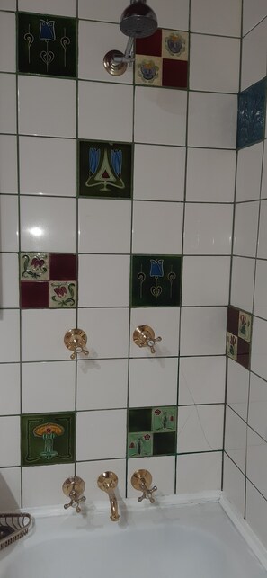 A bathroom with a tiled wall featuring various decorative tiles and a showerhead. - The Little House in the Blue Mountains (Glenbrook)