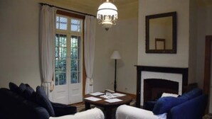 A room with a fireplace, a round table with papers, two blue armchairs, a lamp, and a large mirror on the wall. - The Little House in the Blue Mountains (Glenbrook)