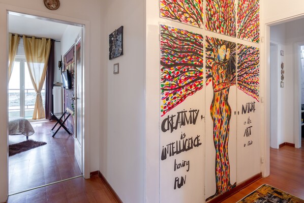 A hallway with a large abstract tree mural, a bed, and a view to a balcony. - Lodge & Art (Trieste)
