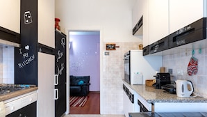 A compact kitchen with black and white cabinetry, a microwave, a kettle, and a toaster. There is a chalkboard with writing on the wall and a small rug on the floor. - Lodge & Art (Trieste)