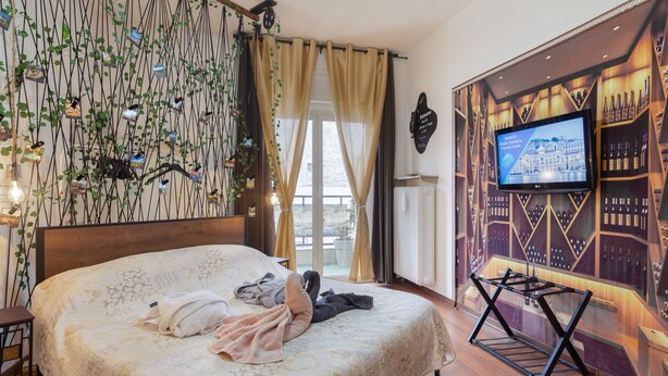 A hotel room with a bed, a TV, a wine rack, and a balcony with plants. - Lodge & Art (Trieste)