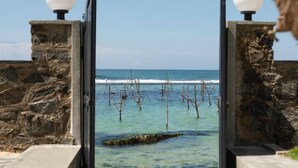 A stone gate with spherical lights, leading to a beach with clear water and wooden structures. - IF Villa in Unawatuna (Unawatuna)