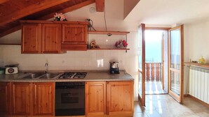 A kitchen with wooden cabinets, a stove, and a sink. There is a balcony with a view of the city.