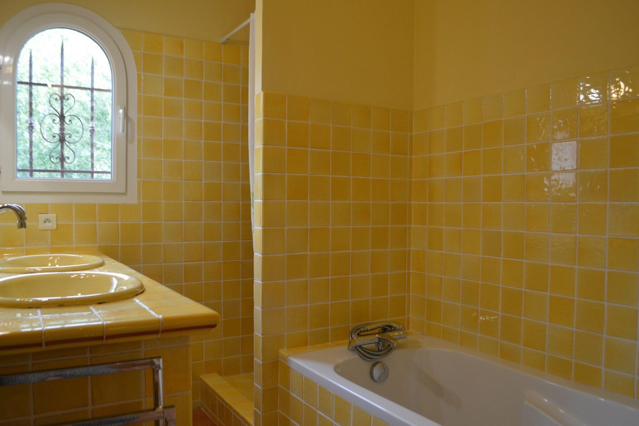 Une salle de bain avec des carreaux jaunes, une fenêtre, un lavabo et une baignoire.