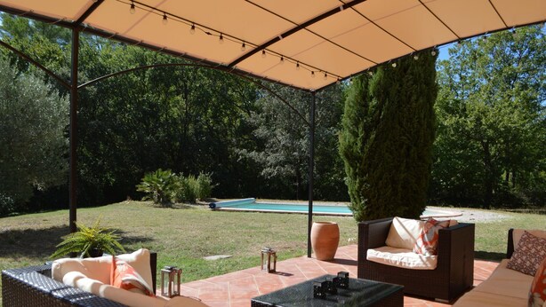 Un espace extérieur aménagé en terrasse, avec des meubles en osier, une piscine et une partie abritée.
