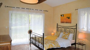 Une chambre à coucher avec un lit, une table de chevet, une lampe, une fenêtre avec des rideaux et un tableau au mur.