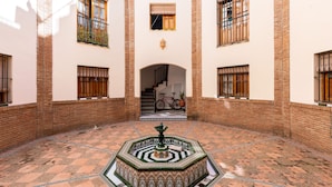 A courtyard with a fountain, tiled floor, and a staircase leading to an upper level.