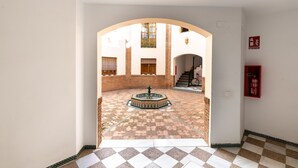 An interior corridor with a checkered floor, a fountain, and a staircase leading to an upper level.