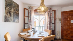 A dining area with a round wooden table, four chairs, a chandelier, and a painting on the wall.