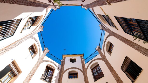 A view of a building with a clear blue sky through the window, featuring multiple balconies and arched windows.