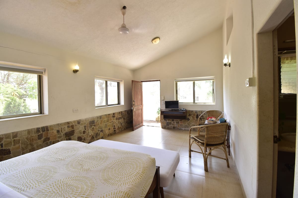A spacious room with a large bed, a stone accent wall, and a seating area with a wicker chair and a small table.