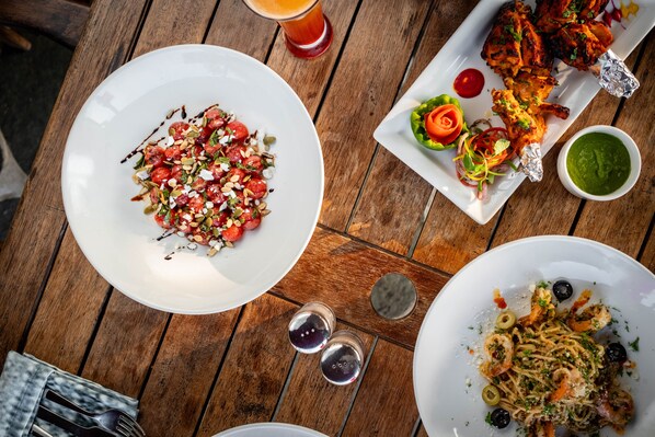 A wooden table with various dishes, including a plate of pasta, a plate of grilled chicken, and a plate of salad. - The Lighthouse (Mumbai)