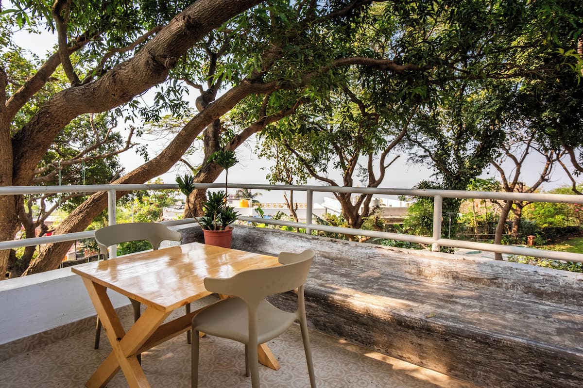 A wooden table and chairs on a balcony with a railing, surrounded by trees and a view of the landscape.