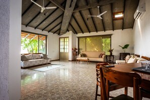 A spacious living area with a high ceiling, large windows, and a dining table. - The Lighthouse (Mumbai)
