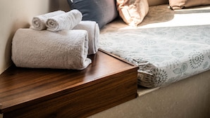 Asiento junto a la ventana con vista a árboles grandes, un banco de madera y toallas enrolladas.