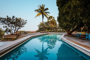 A swimming pool with clear water, surrounded by palm trees and a patio area with chairs and tables. - The Lighthouse (Mumbai)