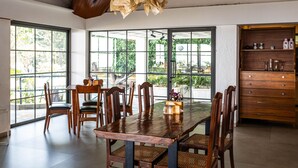 Comedor con mesa y sillas de madera, ventanas amplias y un armario de madera con cajones.