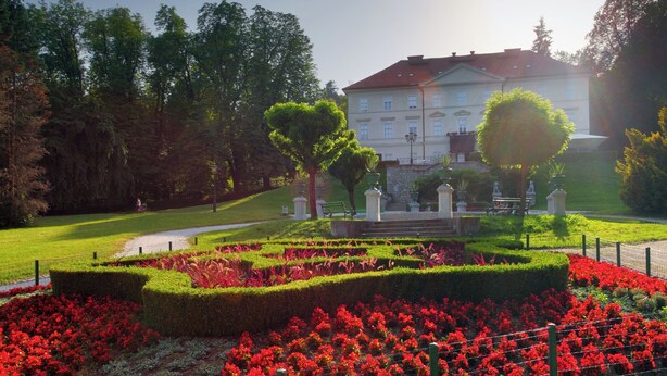 Un jardin à la française, avec des haies taillées avec soin, des fleurs rouges et un bâtiment de style classique en arrière-plan.