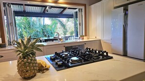 A kitchen with a gas stove, a refrigerator, and a window overlooking greenery. - Magnetic Mango Escape (HORSESHOE BAY)