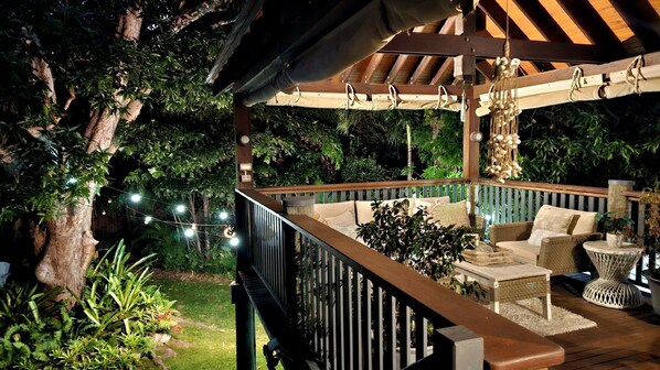 Um terraço ao ar livre com pérgola de madeira, móveis de vime e luzes de corda.