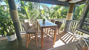 Um deck de madeira com mesa e cadeiras, rodeado por plantas em vasos e palmeiras.