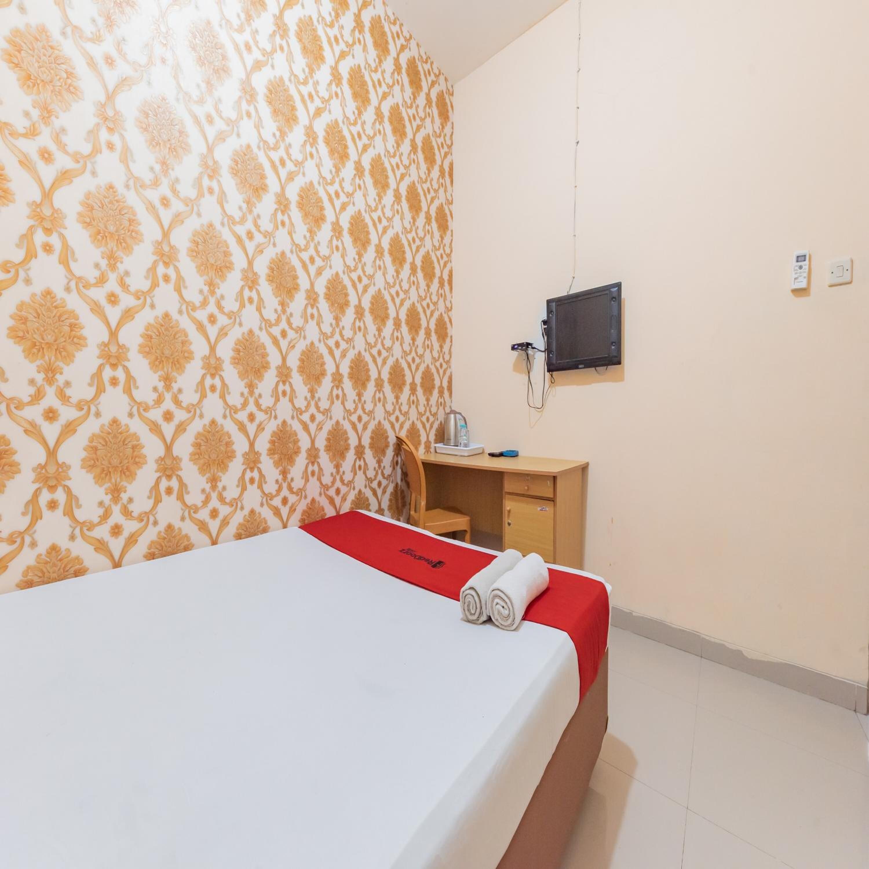 A hotel room with a bed, a desk, a chair, a TV mounted on the wall, and a thermostat.