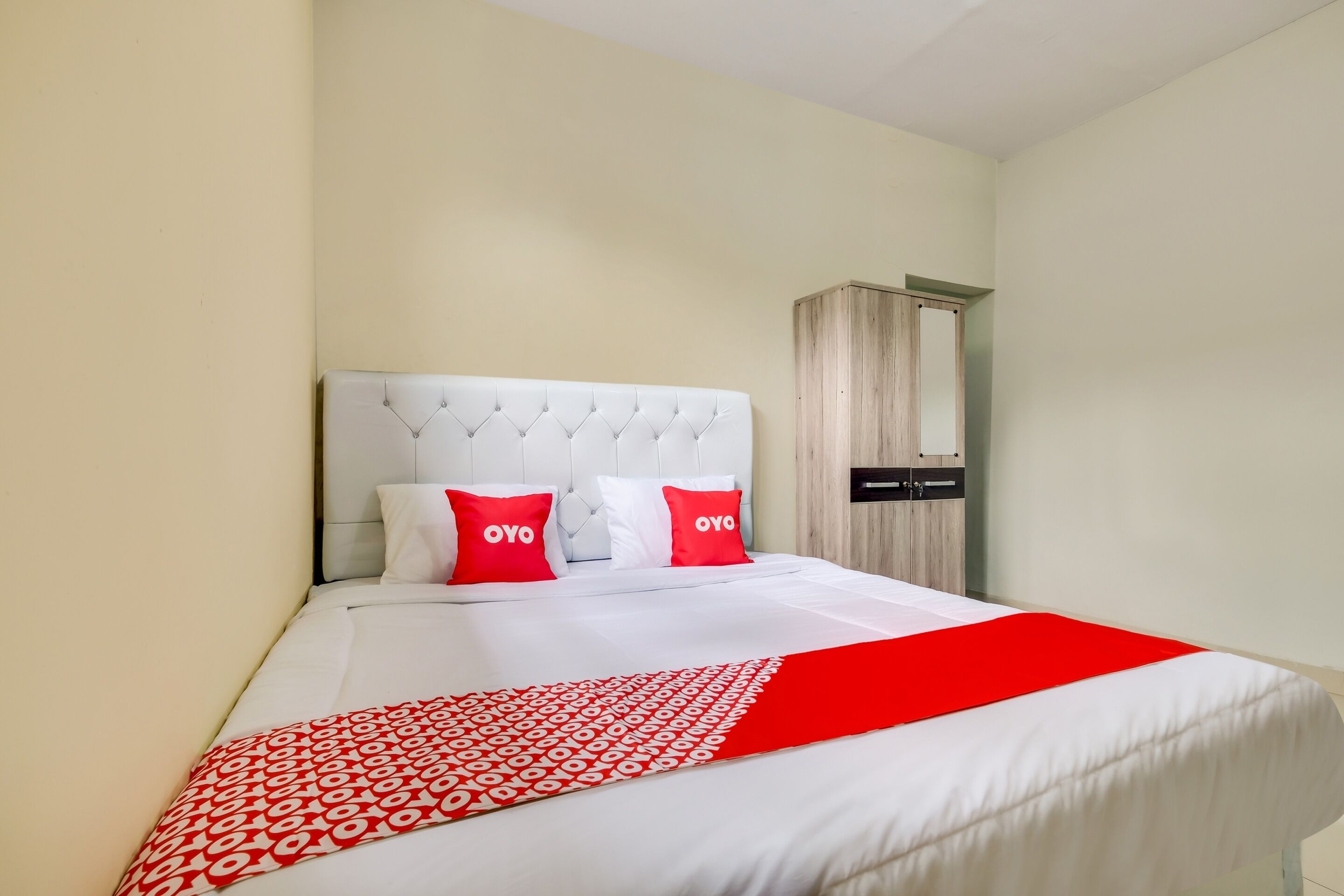 Una habitación de hotel con una cama grande, cabecera blanca y almohadas rojas.